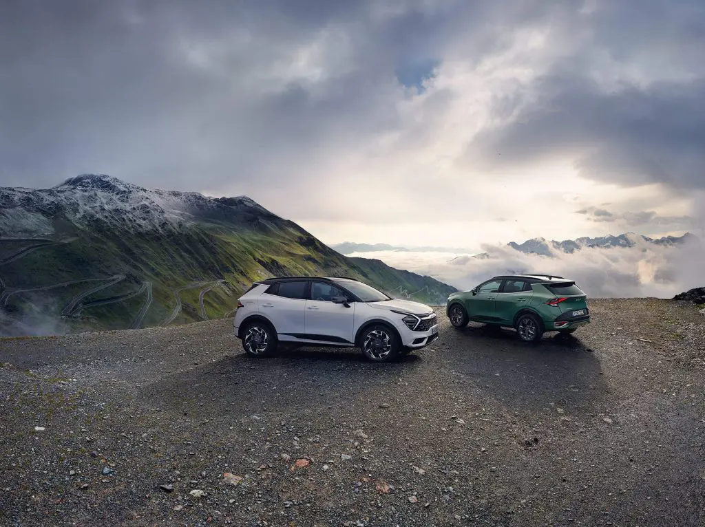 2 Kia Sportage stationné sur un parking en haute montagne. L'un vert l'autre blanc